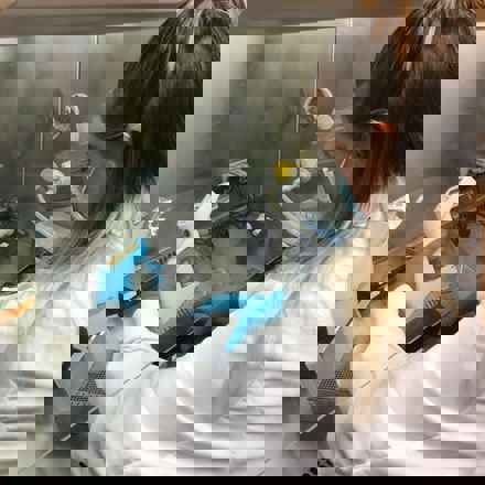 Elisha Griffin in the lab wearing a white lab coat, a face mask, and blue gloves, holding a scanner for an experiment