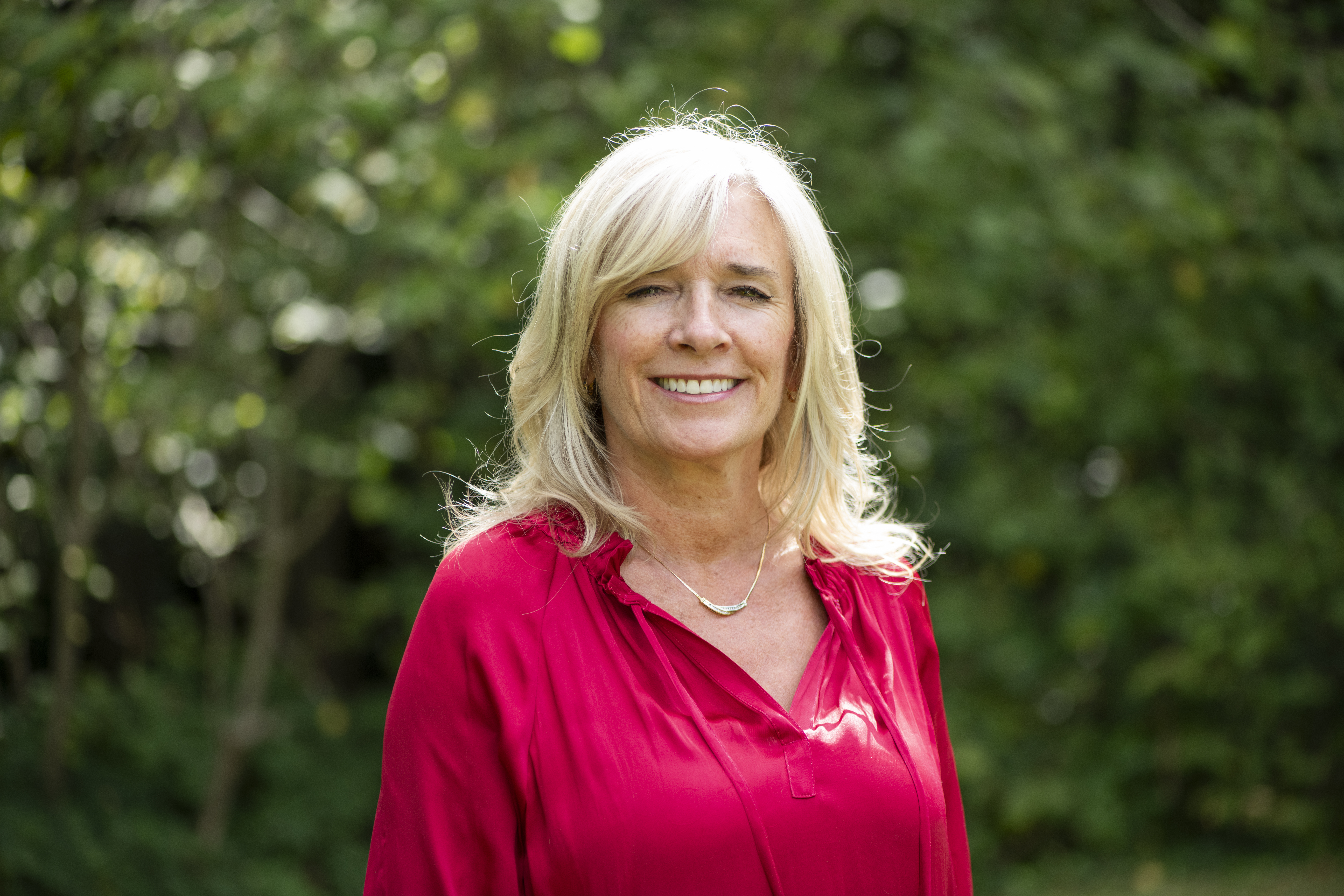 Headshot of Suzanne a white woman with long blonde hair wearing a bright pink blouse