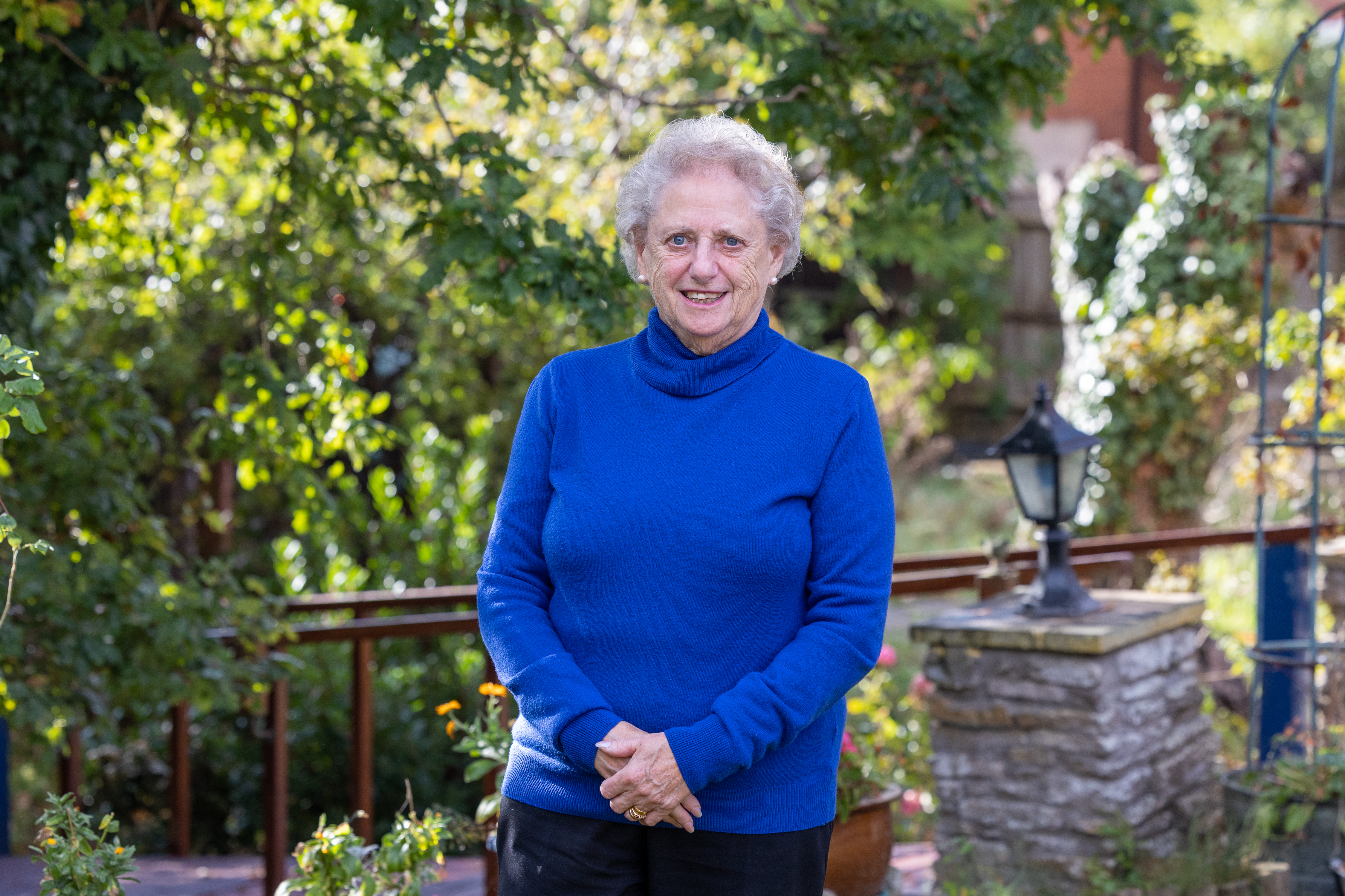 Vera wearing a blue jumper standing in her garden