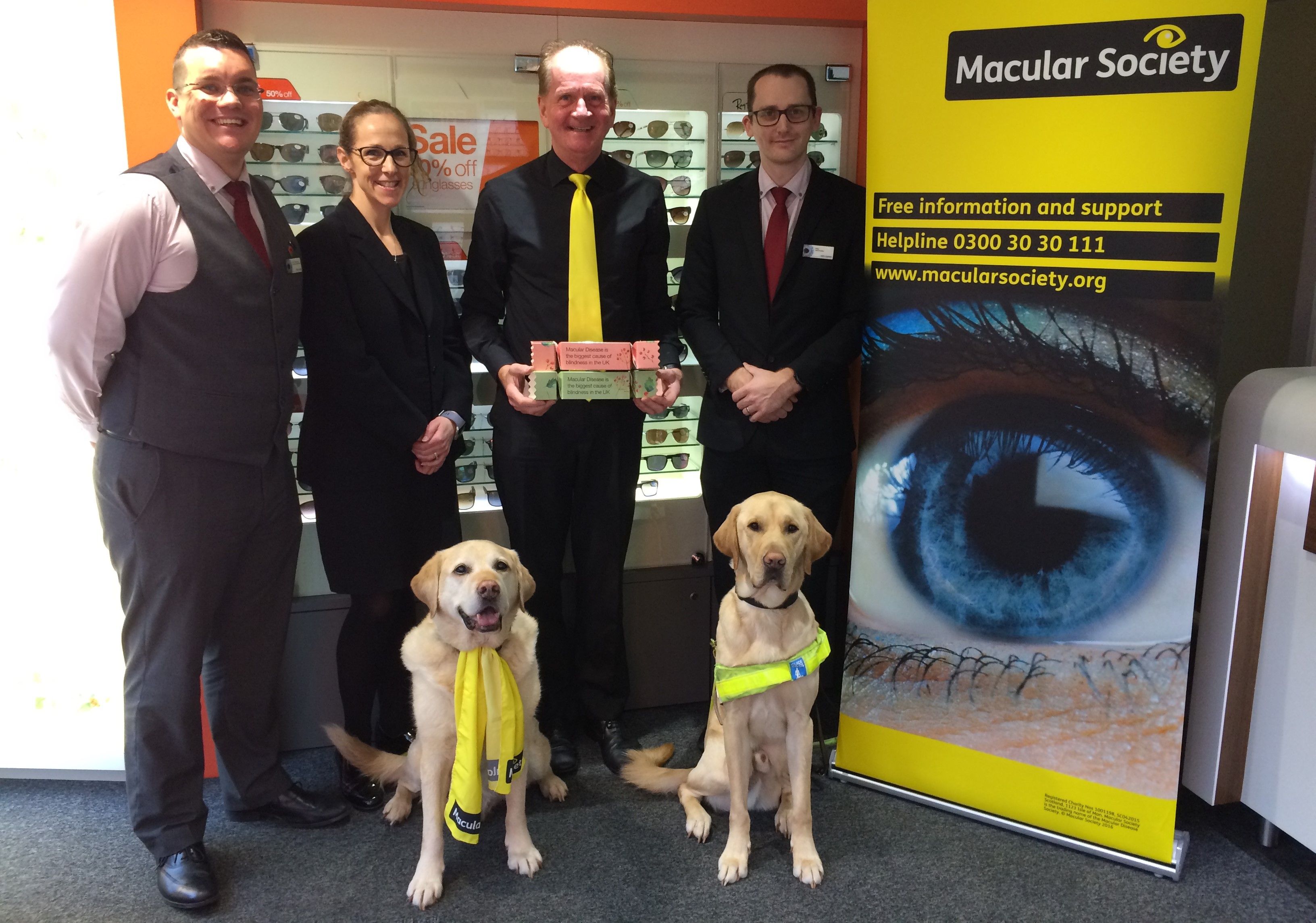Vision Express Lymington - four staff members smiling with two guide dogs and Macular Society sign 