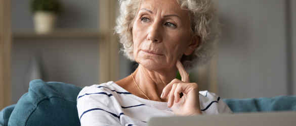 Aged Woman Sitting On Sofa With Laptop Looking Away