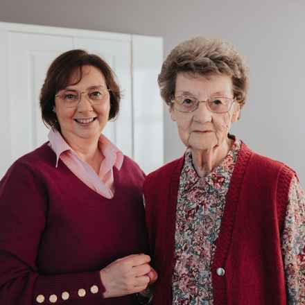 Ann, left, wearing a red cardigan over a pink shirt, holds onto her mum Ruth, wearing a multicoloured shirt under a red cardi.